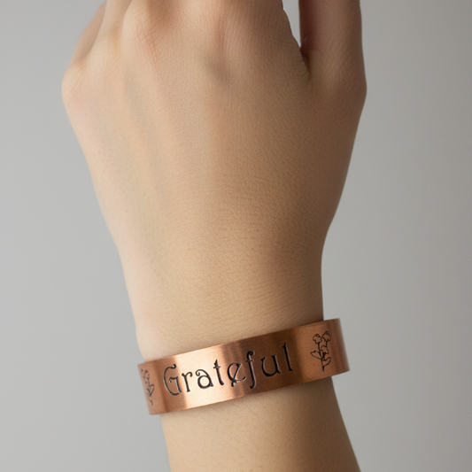 Copper bracelet with engraved text on a wrist against a gray background
